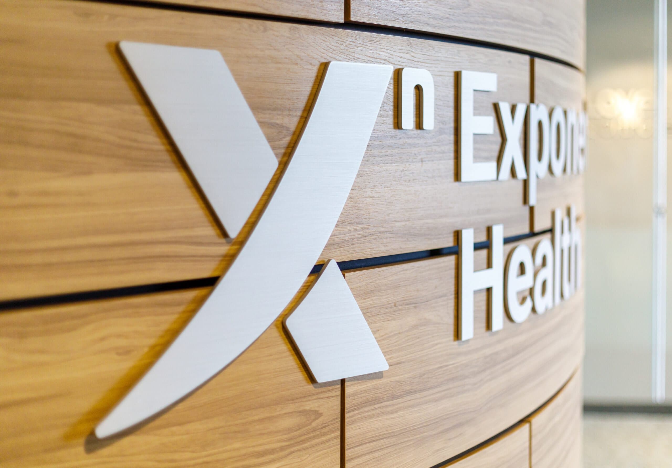 Close-up of a wall sign with the logo and partial text "Exponent Health" on a wood-paneled wall.